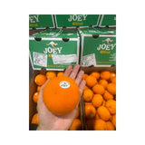 Orange held by a hand with 'JOEY' branded boxes in the background