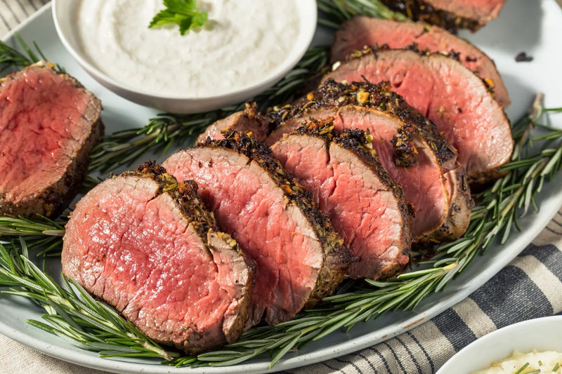 Sliced beef with rosemary on a plate with a side of sauce.